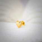 Close-up of heart-shaped 18K nose pin gold placed on a soft white surface highlighting its textured detailing